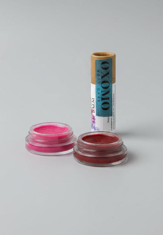 Makeup products including lipsticks and powders on a wooden tray with a white fabric background.