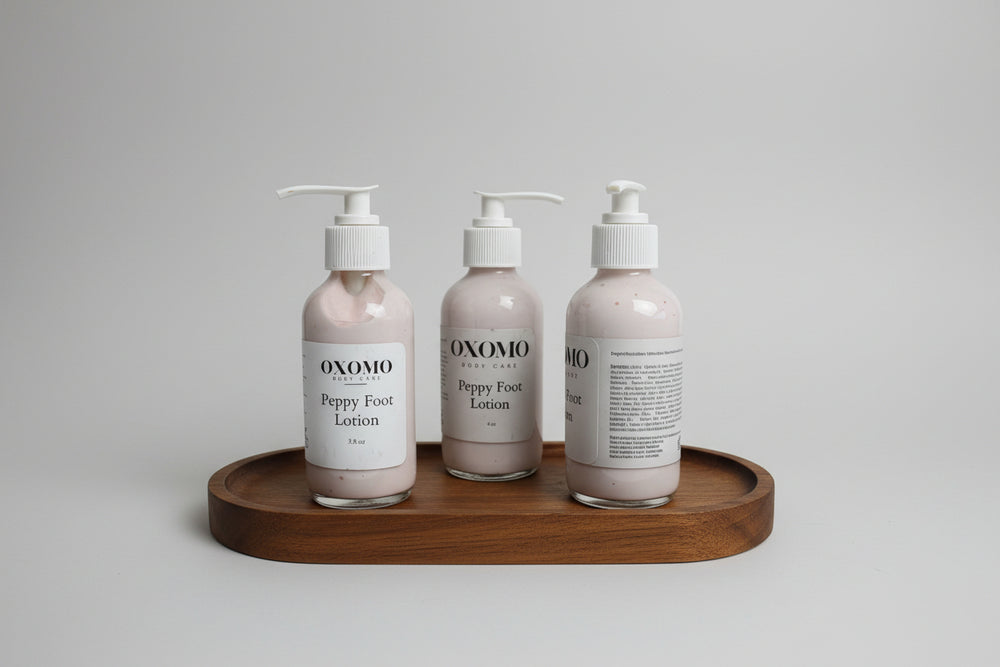 Three bottles of OXOMO Peppy Foot Lotion on a wooden tray with a blurred background.
